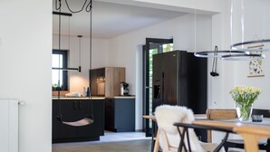 A modern kitchen with a hanging chair, a dining table with chairs, and a refrigerator.