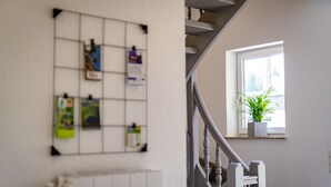 A staircase with a handrail, a bulletin board with various notices, and a window with a plant.