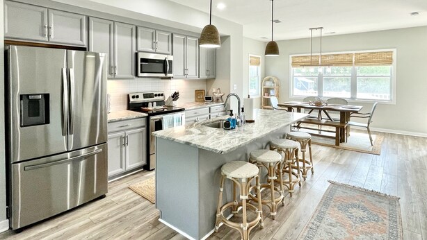 A modern kitchen with stainless steel appliances, a central island with bar stools, and a dining area with a view of the outdoors. - Potomac Paradise - Water views within short walk to Colonial Beach, VA (Colonial Beach)