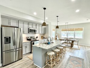 Uma cozinha moderna com eletrodomésticos de aço inoxidável, uma ilha central com banquetas e uma área de refeições com vista para o exterior.