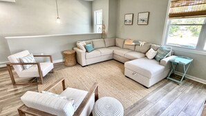 A modern living room with a sectional sofa, a wooden chair, a small side table, and a large window with blinds. - Potomac Paradise - Water views within short walk to Colonial Beach, VA (Colonial Beach)