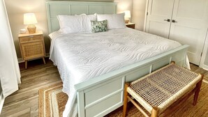 A bedroom with a bed, bedside tables, a ceiling fan, a woven bench, and a door. - Potomac Paradise - Water views within short walk to Colonial Beach, VA (Colonial Beach)