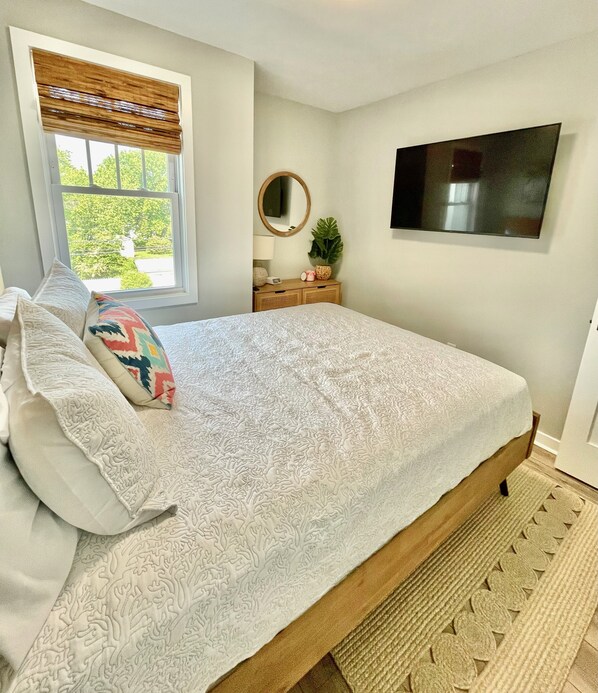 A bedroom with a bed, pillows, a bedside table, a mirror, a television, and a window with blinds. - Potomac Paradise - Water views within short walk to Colonial Beach, VA (Colonial Beach)