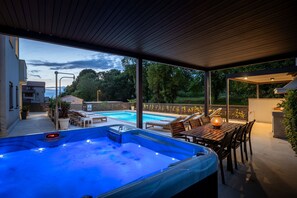 Una bañera de hidromasaje con una mesa y sillas de madera, una piscina y vistas del entorno.