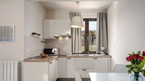 A modern kitchen with white cabinets, a microwave, a kettle, and a window with curtains.