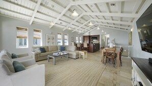 A spacious living area with high ceilings, a dining table, and a kitchen in the background.