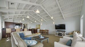 A spacious living area with a high ceiling, a dining set, and a television.