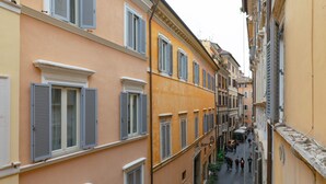 Una stretta via fiancheggiata da edifici con numerose finestre e persiane, un percorso in lastricato e passanti.