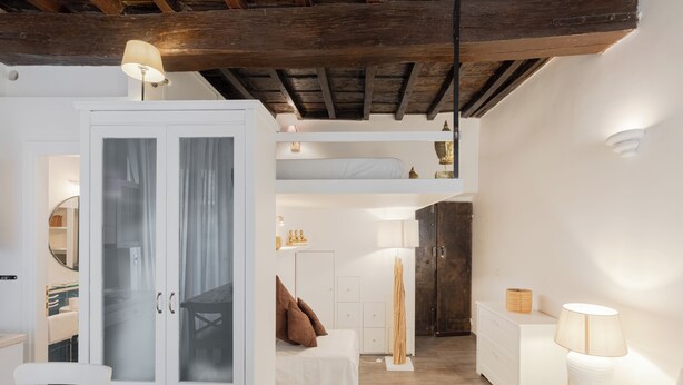 Una camera da letto compatta e moderna con un letto a castello, un'armadio bianco e un comodino con una lampada.