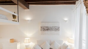 Un divano bianco con cuscini, un comodino con una lampada, un'opera d'arte appesa al muro e un pavimento in legno.