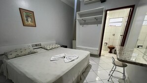 A bedroom with a bed, a bedside table, a hanging coat rack, and a bathroom visible through an open door. - Hotel Mangabeiras Express (Maceió)