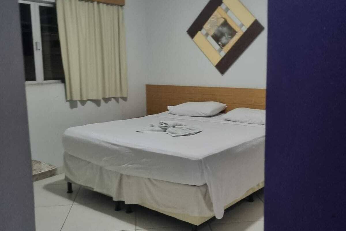 Ein Schlafzimmer mit Bett, einem Fenster mit Vorhängen, einem Wandbild und einer Deckenleuchte.
