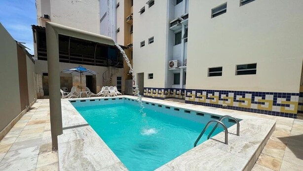 A rectangular swimming pool with a tiled deck, surrounded by a building with a tiled border and a balcony. - Hotel Mangabeiras Express (Maceió)