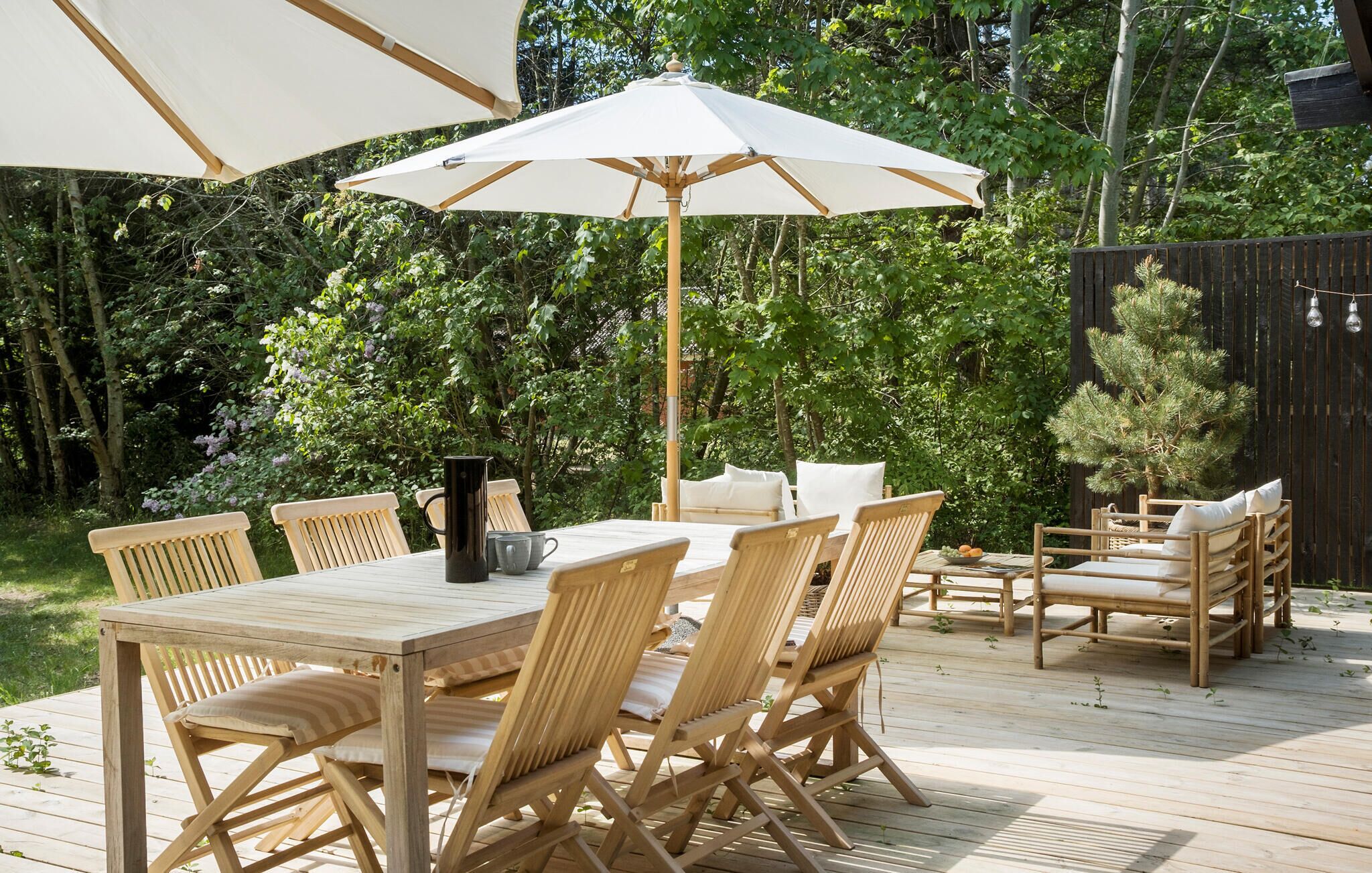 Eine Terrasse aus Holz mit Tisch und Stühlen, umgeben von einem Holzzaun und Bäumen.