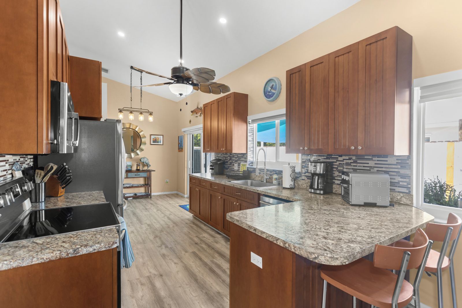 A modern kitchen with granite countertops, wooden cabinets, a built-in oven, and a ceiling fan.