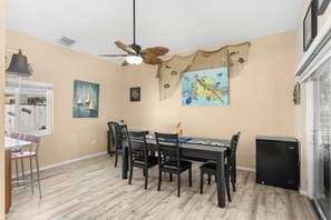 Un espace repas comprenant une table, des chaises, un ventilateur de plafond et des œuvres d’art accrochées aux murs.