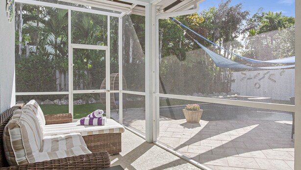 A sunroom with a view of a garden, a wicker sofa, and a potted plant.