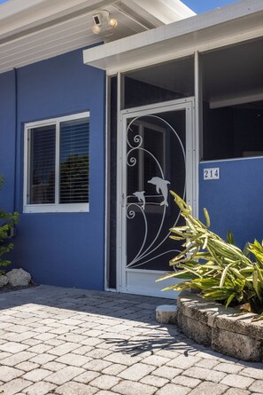 Un bâtiment à la façade bleue, une porte blanche ornée d’un motif métallique et le numéro « 214 » inscrit sur le mur.