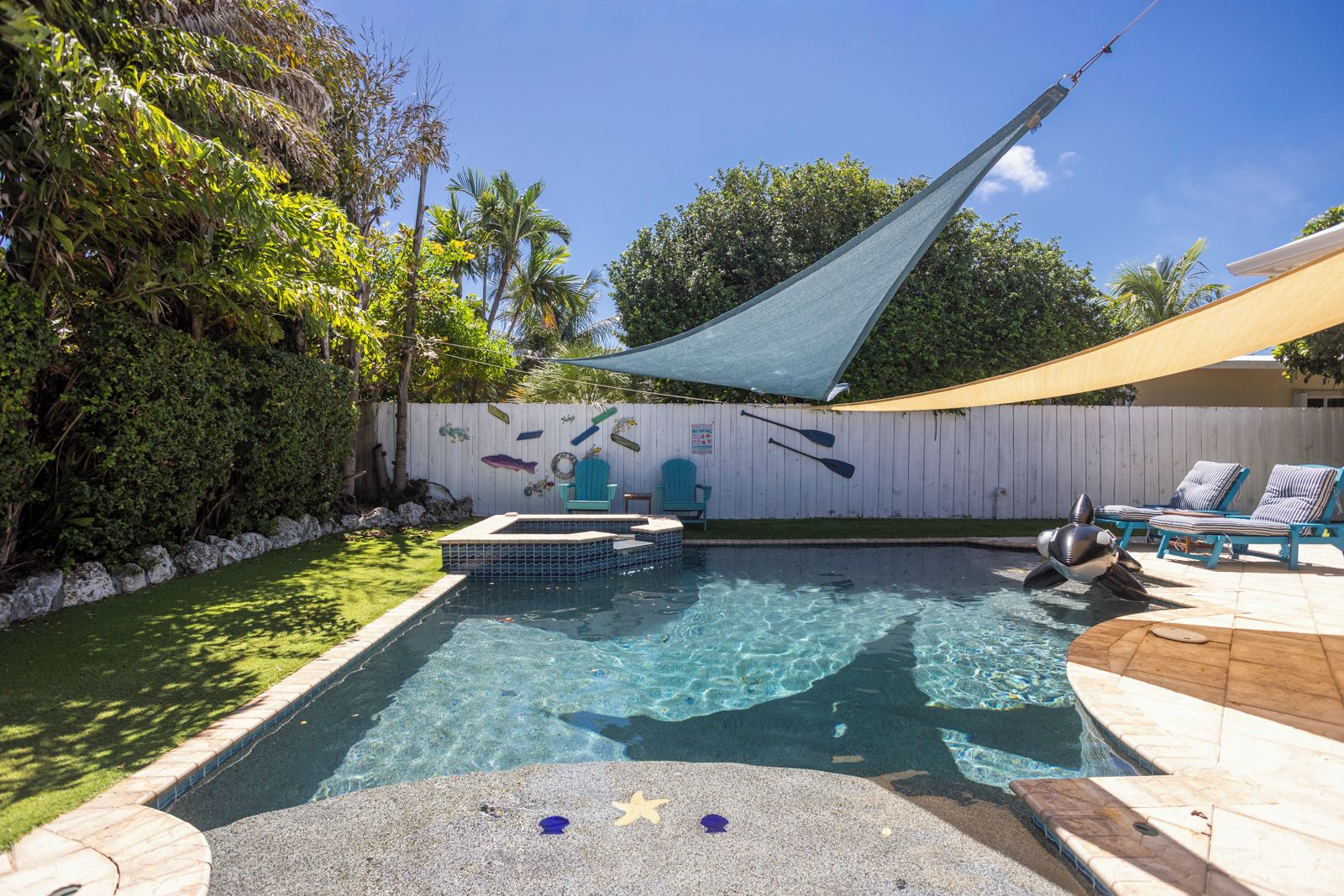 A swimming pool with a small hot tub, lounge chairs, and a shaded area.