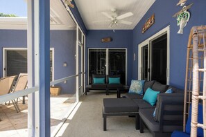 A covered outdoor seating area with a ceiling fan, a sofa with cushions, and a wicker chair. - Superb Keys home w/heated pool, jacuzzi, fast wifi & more! (Tavernier)