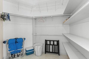 Un coin de pièce avec un étagère métallique, un sac bleu, une poubelle blanche et une barrière de sécurité noire pour bébé.