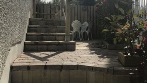 Eine Steintreppe führt zu einem Holzbalkon mit weißen Stühlen und einem Holzzaun.