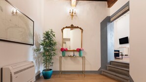 Een gang met een houten vloer, een plant in een pot, een spiegel op een console en een trap.