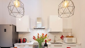 Een moderne keuken met witte kastjes, een centraal eiland met een wijnfles, en twee hangende hanglampen.
