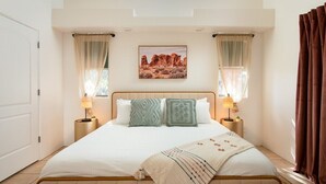 A bedroom with a bed, two bedside lamps, a window with curtains, and a painting on the wall. - Enchanted Adobe Hideaway w/Hot Tub & GIANT Chess (Sedona)