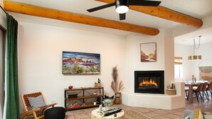 A living room with a fireplace, a dining area, and a painting of a landscape. - Enchanted Adobe Hideaway w/Hot Tub & GIANT Chess (Sedona)