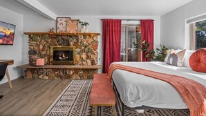 Ein Schlafzimmer mit Kamin aus Stein, einem Bett mit weißer Bettwäsche, einer Bank und einem gemusterten Teppich.