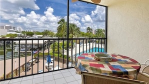 A balcony with a view of a swimming pool and palm trees, a ceiling fan, and a table with a colorful tablecloth.