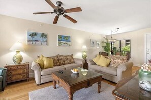Ein Wohnzimmer mit zwei Sofas, einem Couchtisch, einem Deckenventilator und Wandbildern.