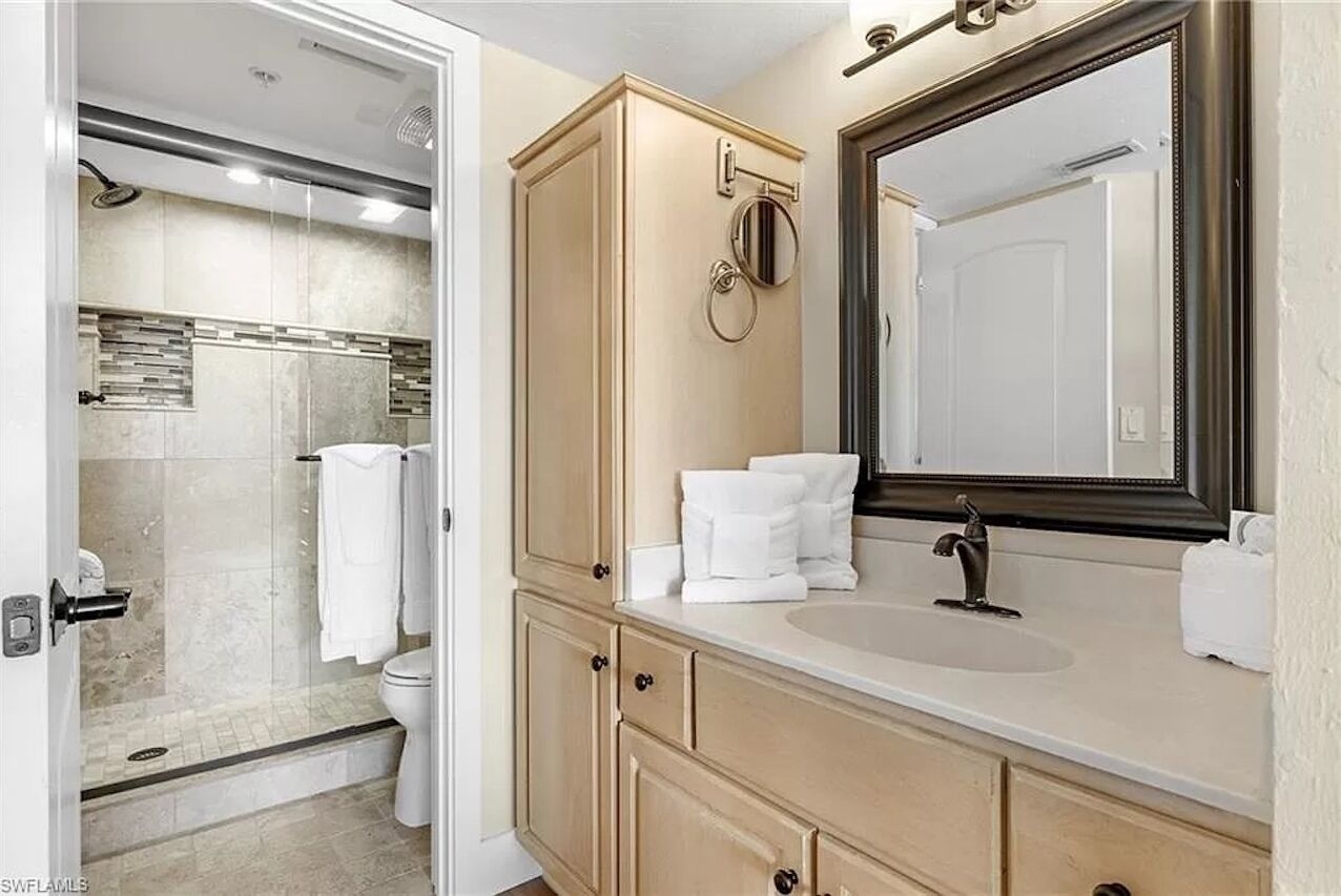 A modern bathroom with a glass shower enclosure, a beige vanity with a large mirror, and a white sink.
