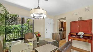 A dining area with a glass table, chairs, and a vase of flowers. There is a red cabinet and a hanging light fixture above the table.