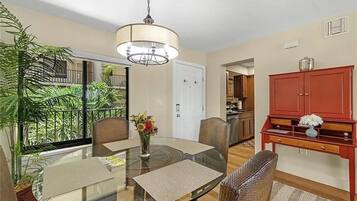 A dining area with a glass table, chairs, and a vase of flowers. There is a red cabinet and a hanging light fixture above the table.