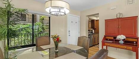 A dining area with a glass table, chairs, and a vase of flowers. There is a red cabinet and a hanging light fixture above the table.