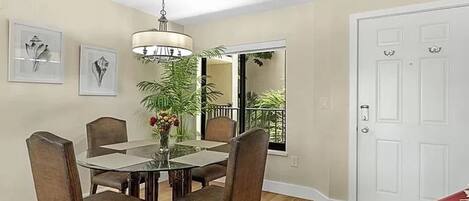 A dining area with a round table, six chairs, a chandelier, and a potted plant.