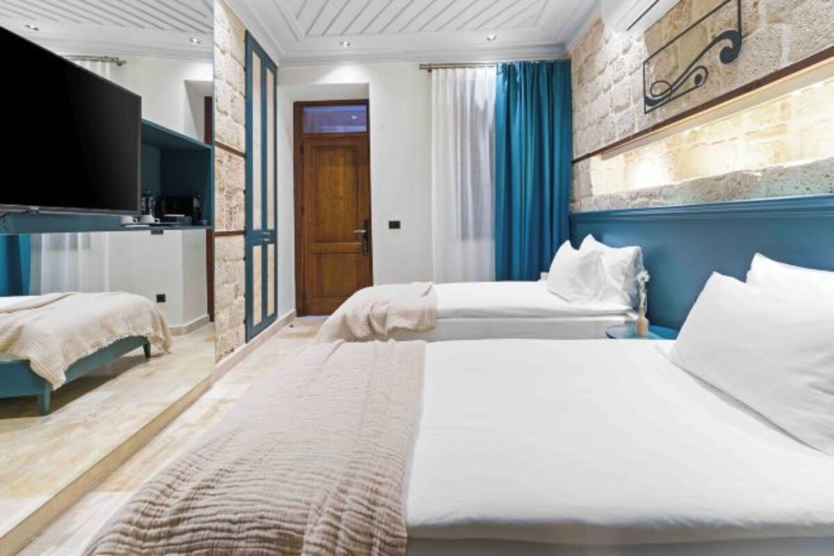 A hotel room with two beds, a flat-screen TV, a brick accent wall, and a wooden door.