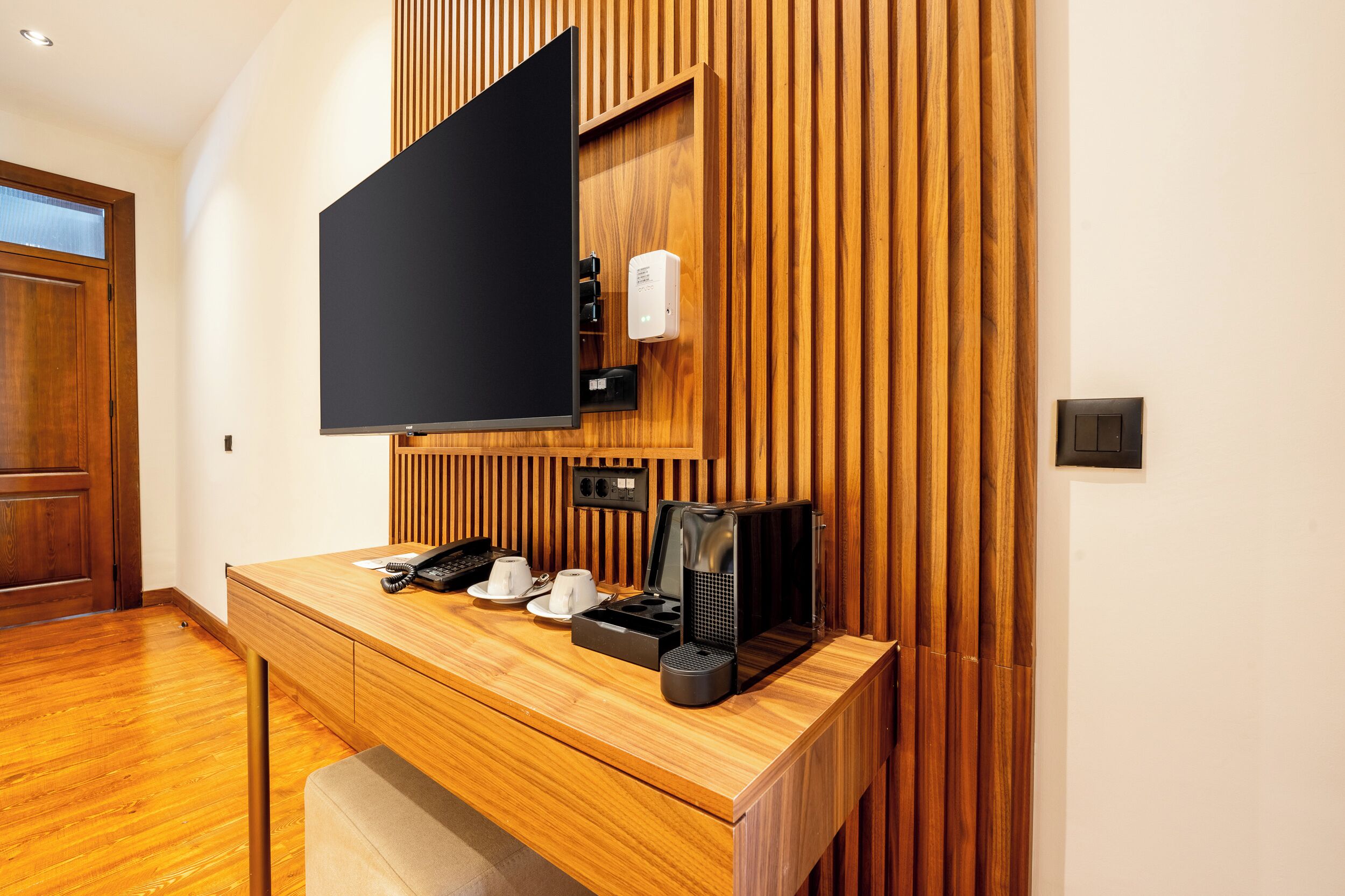 Una habitación de hotel moderna con un escritorio de madera, un televisor de pantalla plana, una cafetera y un teléfono.