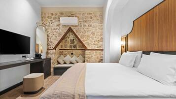 Un dormitorio con pared de piedra, cabecero de madera, televisor de pantalla plana, mesita de noche y cama con ropa blanca.