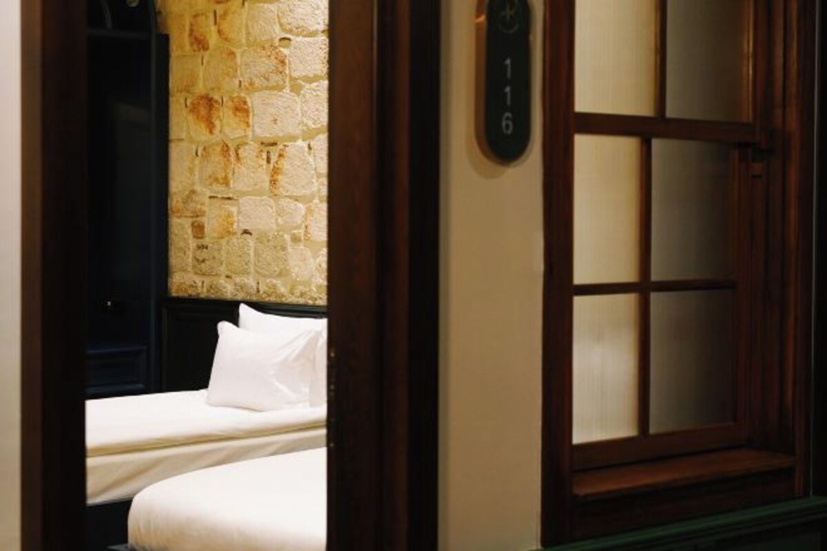 A hotel room with a stone wall, a bed with white bedding, and a wooden door with a number plate.