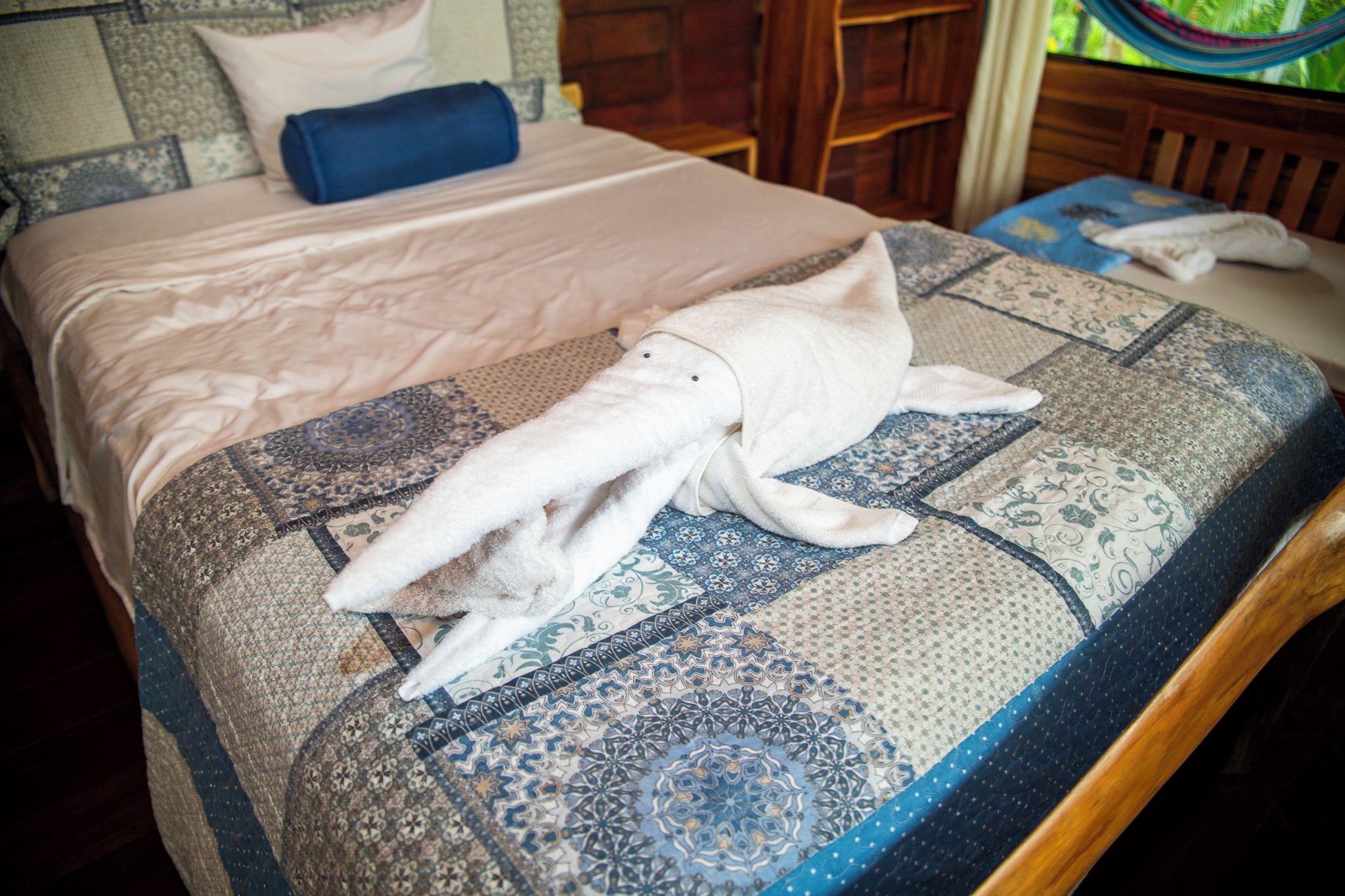 A bed with a patterned bedspread and a rolled towel on it.