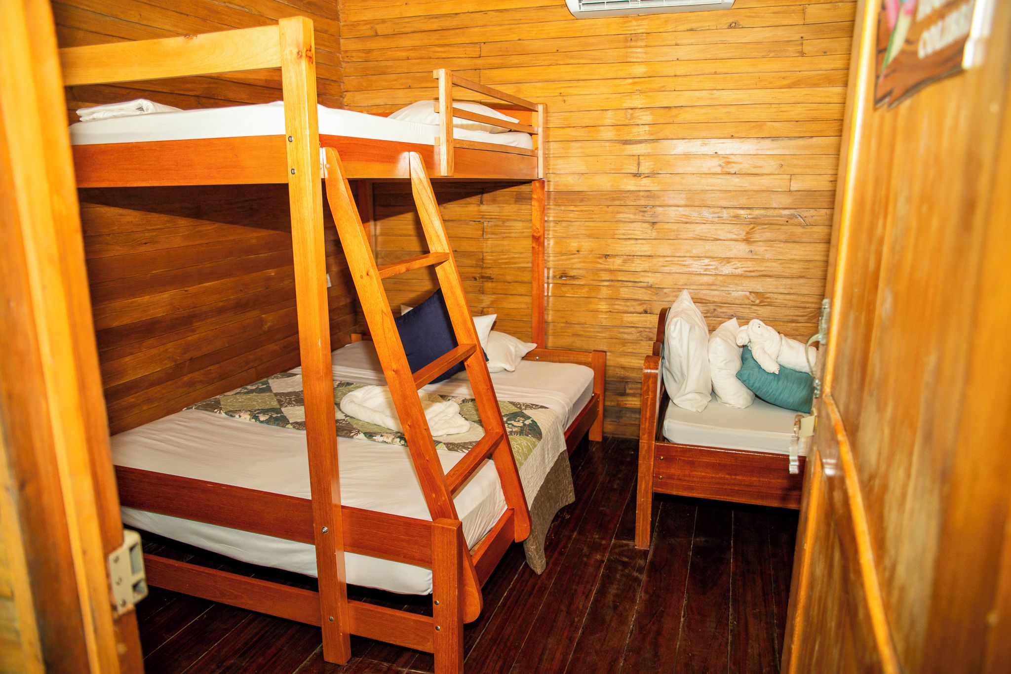 A wooden bunk bed room with a ladder, a small table, and pillows.