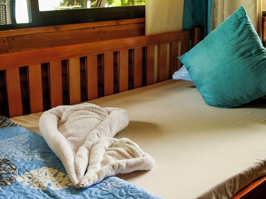 A bed with a blue quilt, a white towel, and a teal pillow.