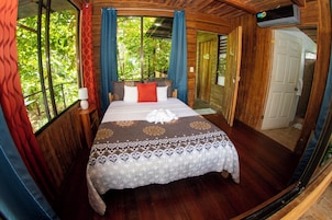 Una cama con una colcha estampada, una lámpara de noche y una ventana con cortinas.
