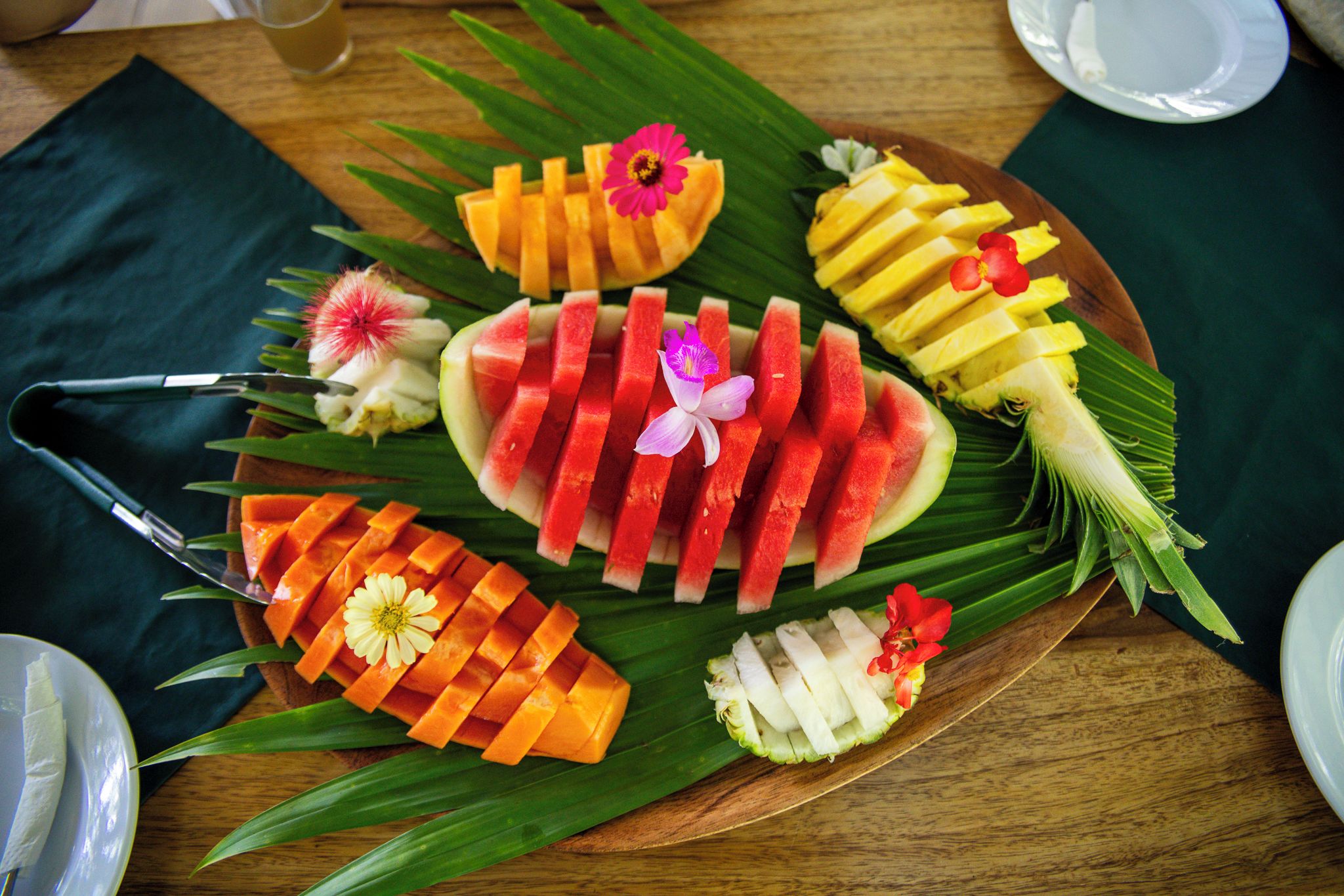 A wooden table with a fruit platter arranged on a banana leaf.
