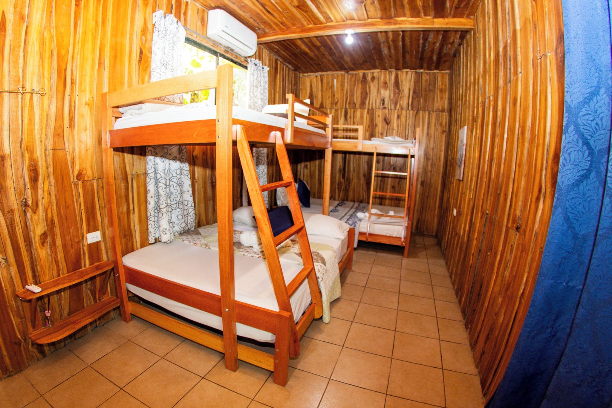 Un interior de madera con literas, suelo de baldosas y una cortina.