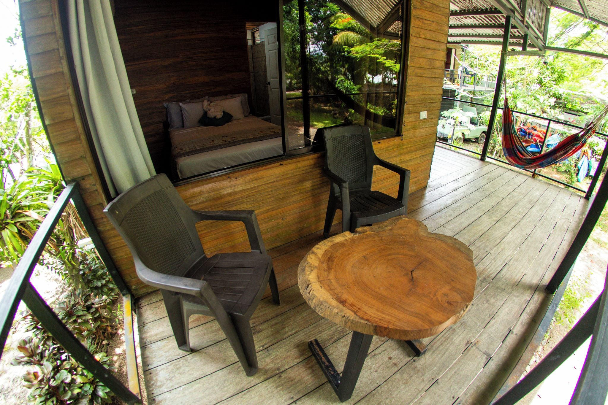A wooden deck with a round table and two chairs, a hammock, and a view of the surrounding greenery.