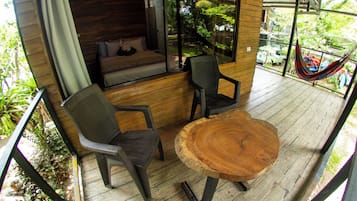 A wooden deck with a round table and two chairs, a hammock, and a view of the surrounding greenery.